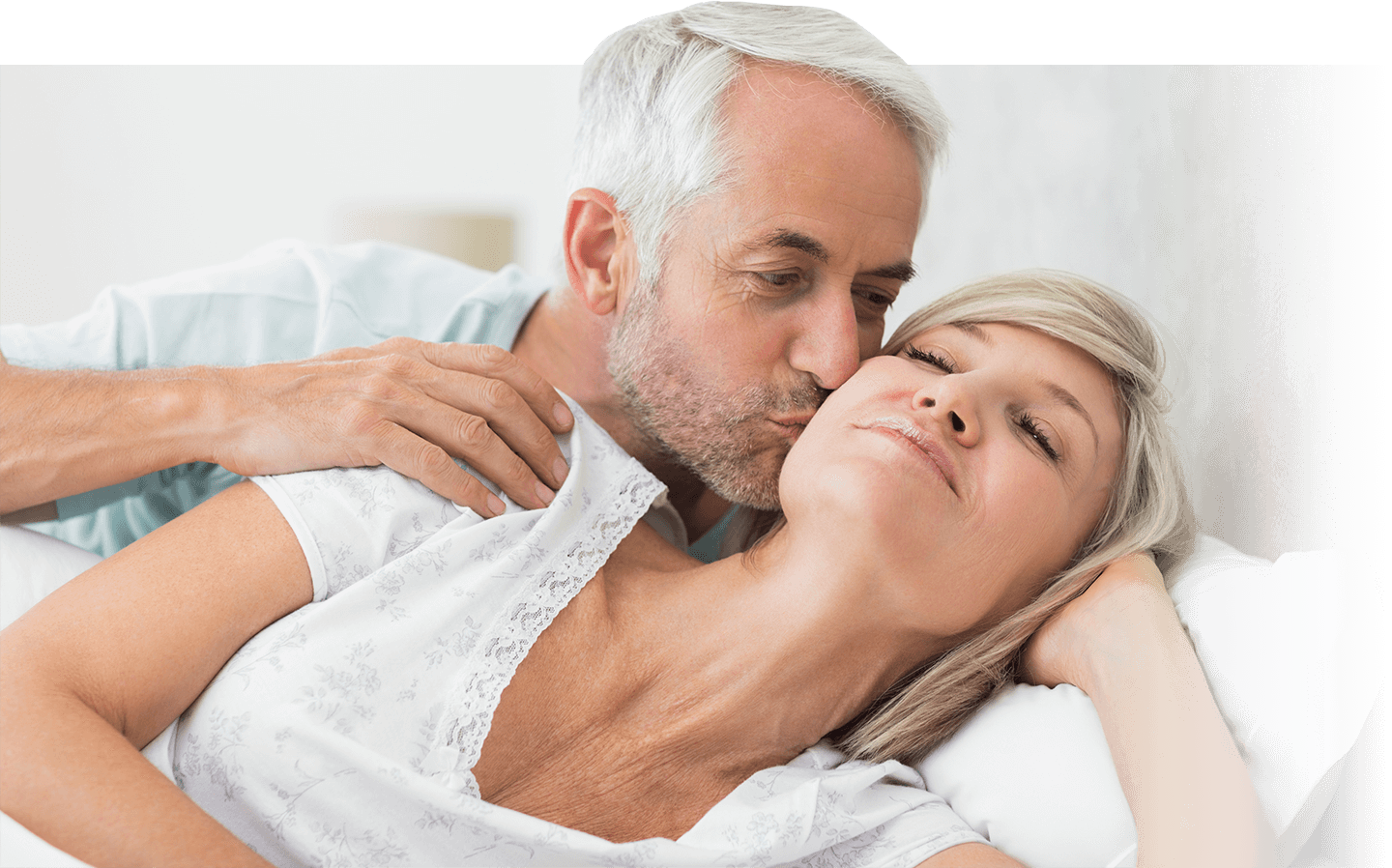 older guy kissing wife on cheek in bed